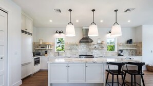 A modern kitchen with white cabinetry, a large island, pendant lighting, and a view of greenery outside.