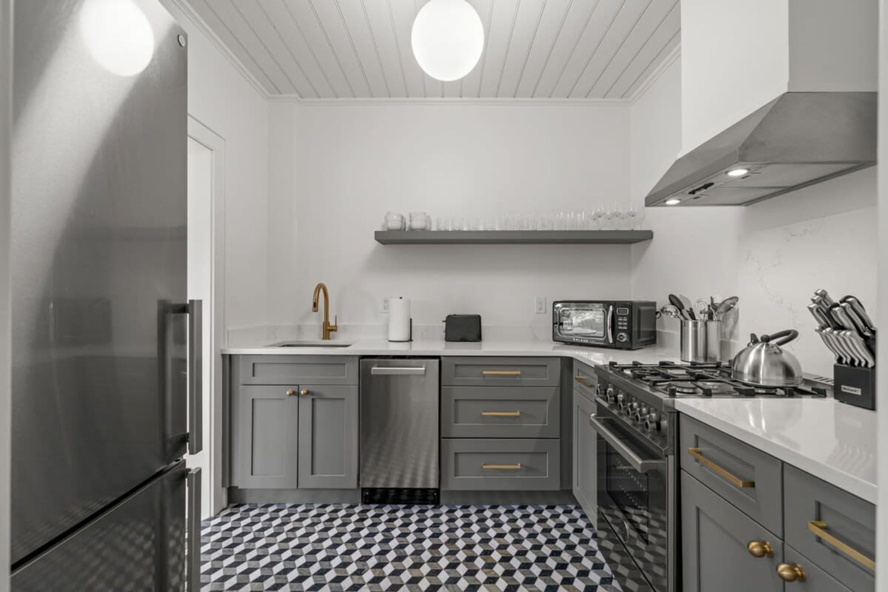 A modern kitchen with grey cabinetry, a black and white checkered floor, a built-in oven, and a microwave.