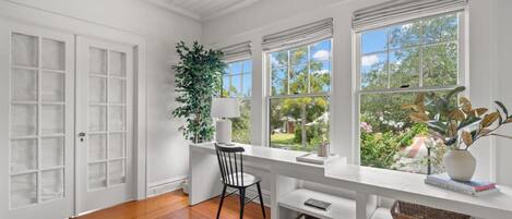 A bright room with white walls, wooden flooring, and large windows offering a view of greenery.