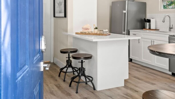 A modern kitchen with white cabinetry, a central island, and a blue door. - Soho Suite by Brightwild Steps to Soho (Tampa)