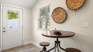 A room with a white door, a window with blinds, a round table with stools, and two woven wall decorations. - Soho Suite by Brightwild Steps to Soho (Tampa)