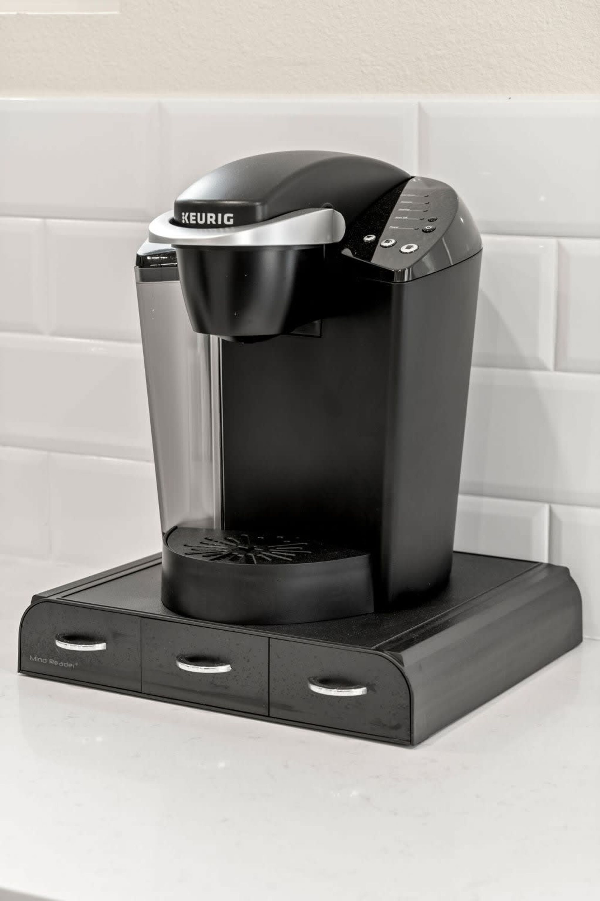 A Keurig coffee machine with a black and silver design, placed on a white countertop.