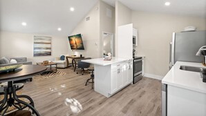 A modern kitchen with white cabinetry, a central island, and a dining area with a round table and chairs. - Soho Suite by Brightwild Steps to Soho (Tampa)