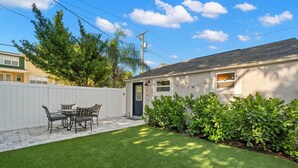 A house with a white exterior, a front door, a small porch with a table and chairs, and a well-maintained lawn. - Soho Suite by Brightwild Steps to Soho (Tampa)