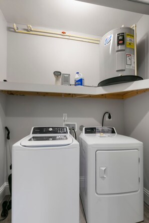A laundry area with two white washing machines and a water heater on a shelf. - Canopy Cove Stunning 2BR Apt Heart of Downtown (Safety Harbor)