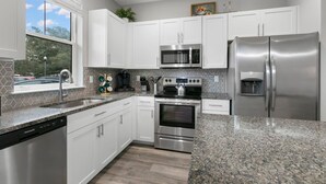 A modern kitchen with white cabinets, stainless steel appliances, a granite countertop, and a window providing a view of the outdoors.