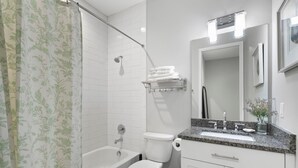 A modern bathroom with a bathtub, toilet, and vanity with a sink and mirror.