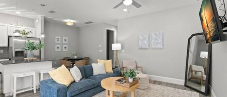 Ein modernes Wohnzimmer mit einem blauen Sofa, einem Holztisch und einem Deckenventilator.