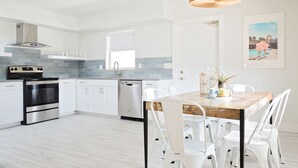 A modern kitchen with white cabinets, stainless steel appliances, and a dining area with white chairs. - Stunning 2BR Suite, Just Steps to the Beach (Clearwater Beach)