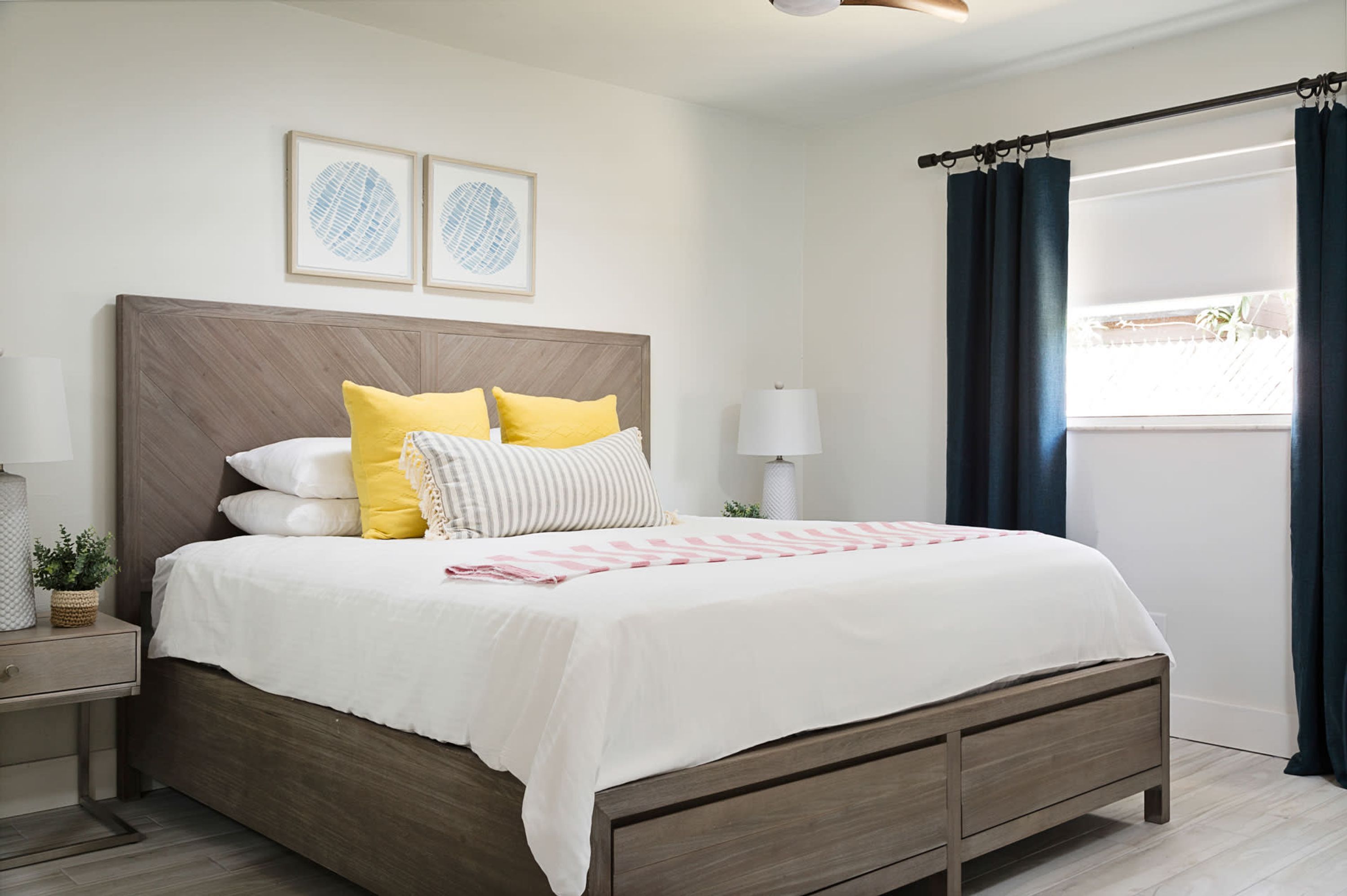 Una cama bien hecha con cabecera de madera, una mesita de noche con lámpara y una ventana con cortinas.