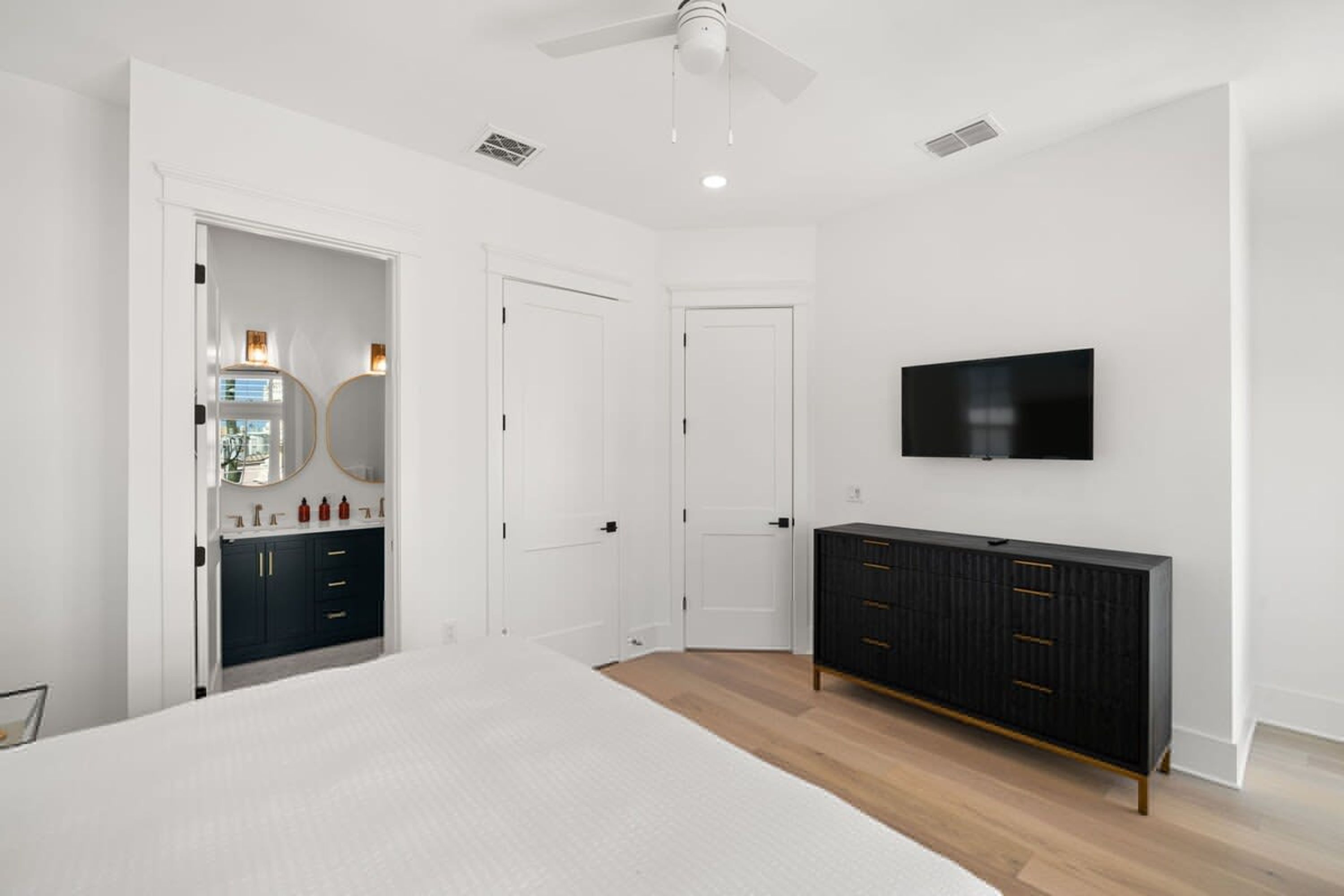 A bedroom with a bed, a dresser, a TV, and a ceiling fan.