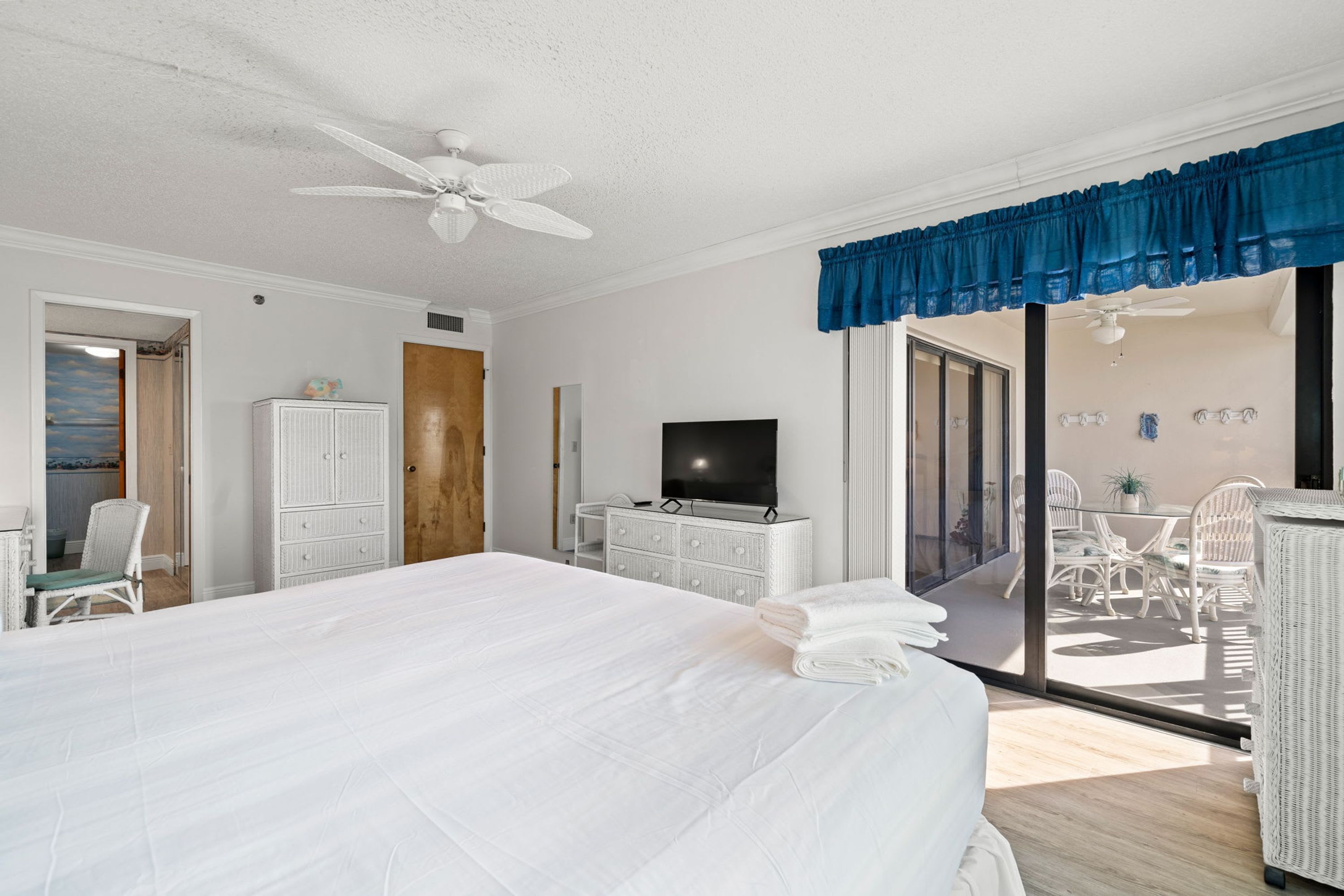 Un dormitorio con cama, televisor, armario y puerta corredera de cristal que da a un espacio exterior con sillas y una mesa.