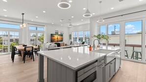 A modern kitchen with a large island, dining area, and large windows offering views of the city. - Jade House at The Gemma (Clearwater Beach)