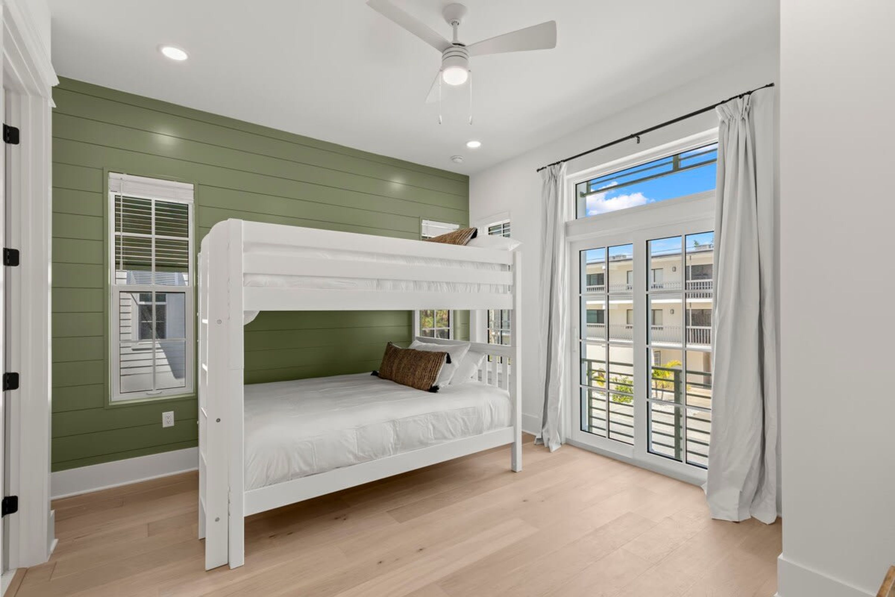 A bunk bed room with a ceiling fan, a window with blinds, and a view of a balcony.