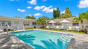 A swimming pool with a white fence, lounge chairs, and palm trees. - Deluxe King Condo Updated Suite by the Beach! (Clearwater Beach)