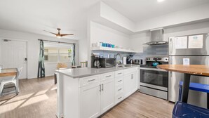 A modern kitchen with white cabinets, stainless steel appliances, and a wooden dining table. - Deluxe King Condo Updated Suite by the Beach! (Clearwater Beach)