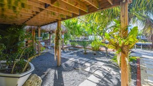 Ett takförsett utomhusområde med en träpergola, krukväxter och en konstruktion med ett halmtak.