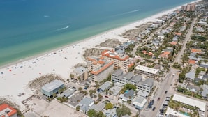 An aerial view of a coastal town with a beach, buildings, and a clear sky.