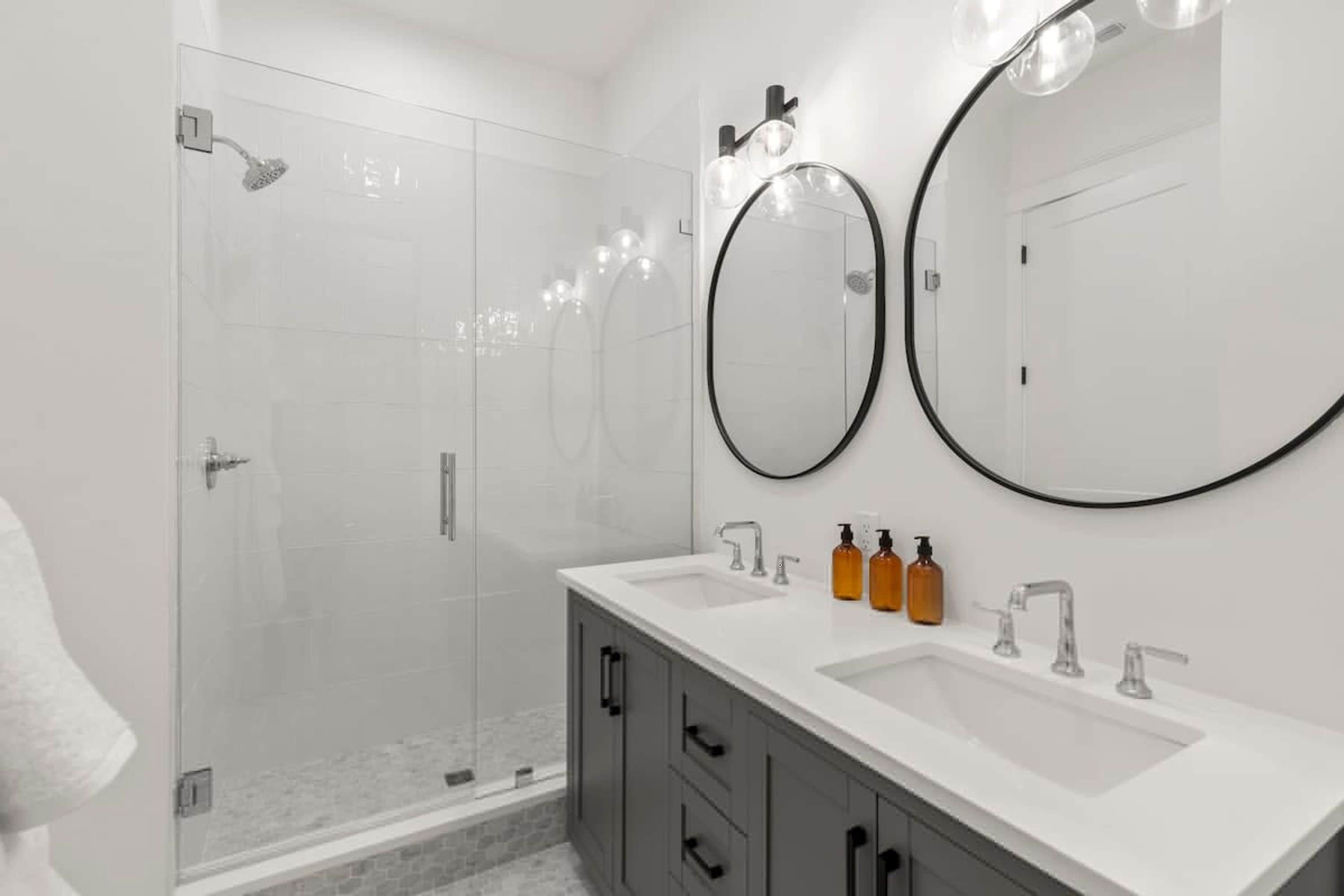 Une salle de bain moderne dotée d’une douche à parois de verre, de deux lavabos et d’un grand miroir.