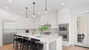 A modern kitchen with white cabinetry, stainless steel appliances, and black bar stools.