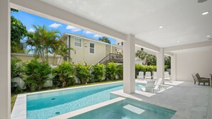 Una piscina con agua cristalina azul, rodeada de abundante vegetación y un edificio blanco al fondo.