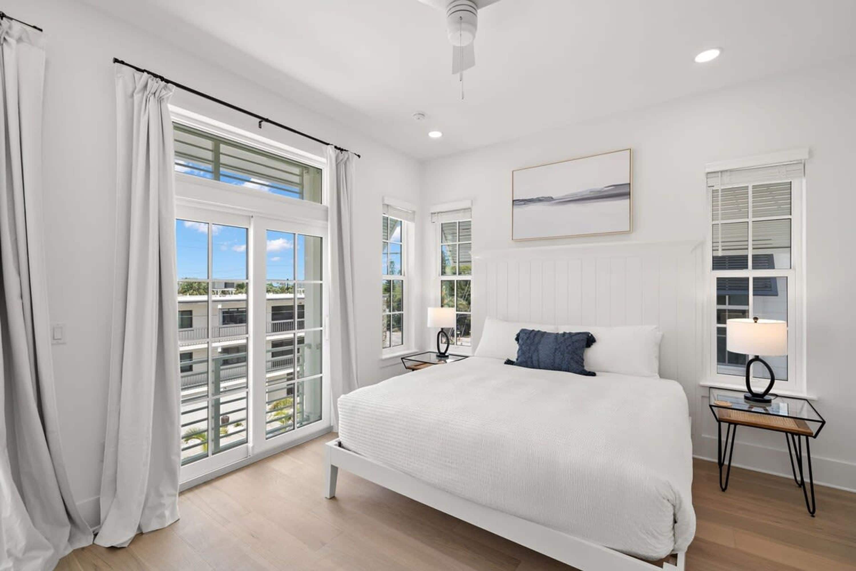 A spacious bedroom with a large bed, a view of the outdoors through a sliding glass door, and a ceiling fan.