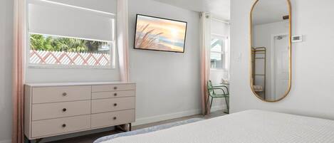 Un dormitorio con una cama, un aparador, un televisor, un espejo y una ventana con cortinas.