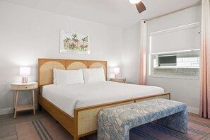 A bedroom with a bed, bedside tables, a bench, a window, and a wall-mounted artwork.
