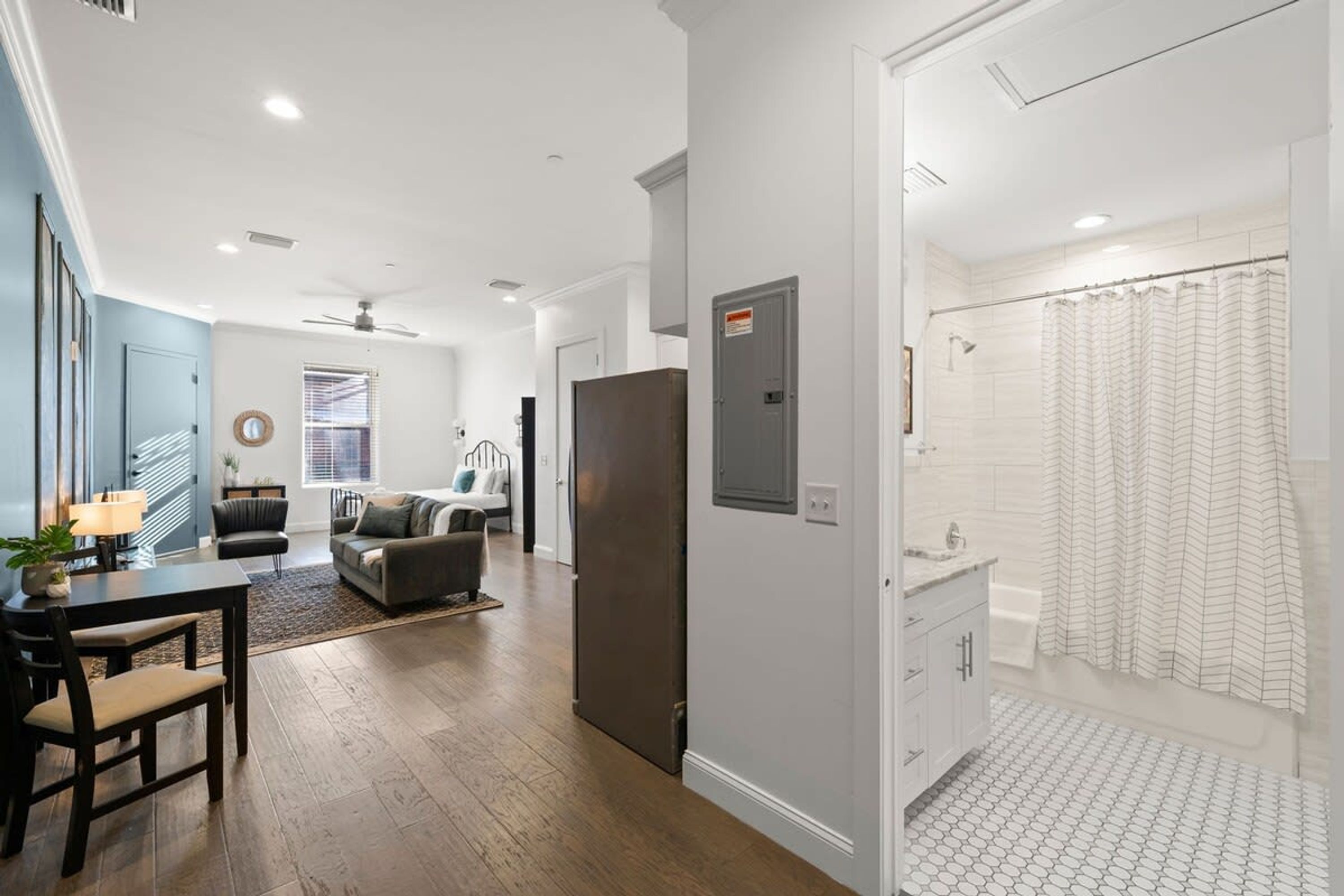 Un salon moderne avec un coin repas, un réfrigérateur gris et une salle de bain avec un rideau de douche.