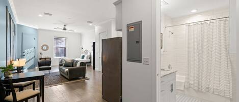 Un salon moderne avec un coin repas, un réfrigérateur gris et une salle de bain avec un rideau de douche.