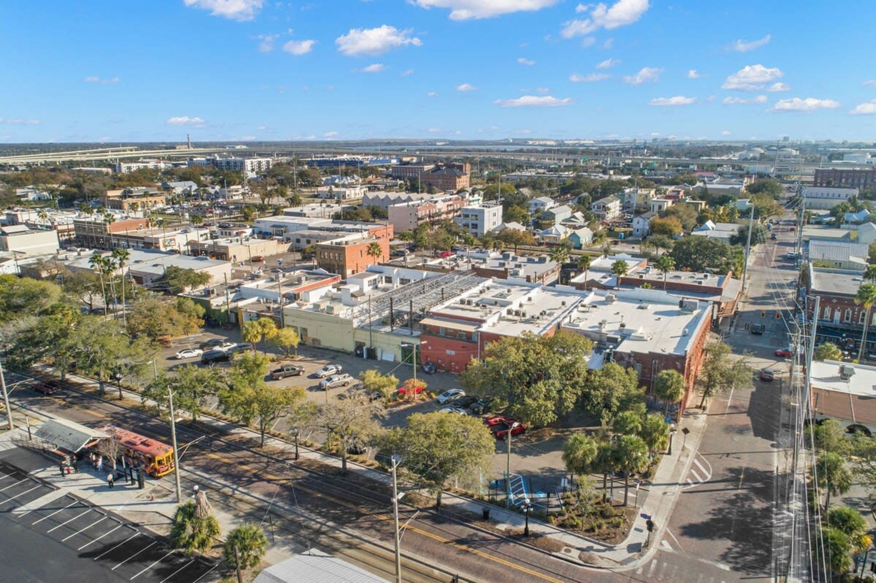 An aerial view of a cityscape with a mix of commercial and residential buildings, a tram line, and a clear sky.