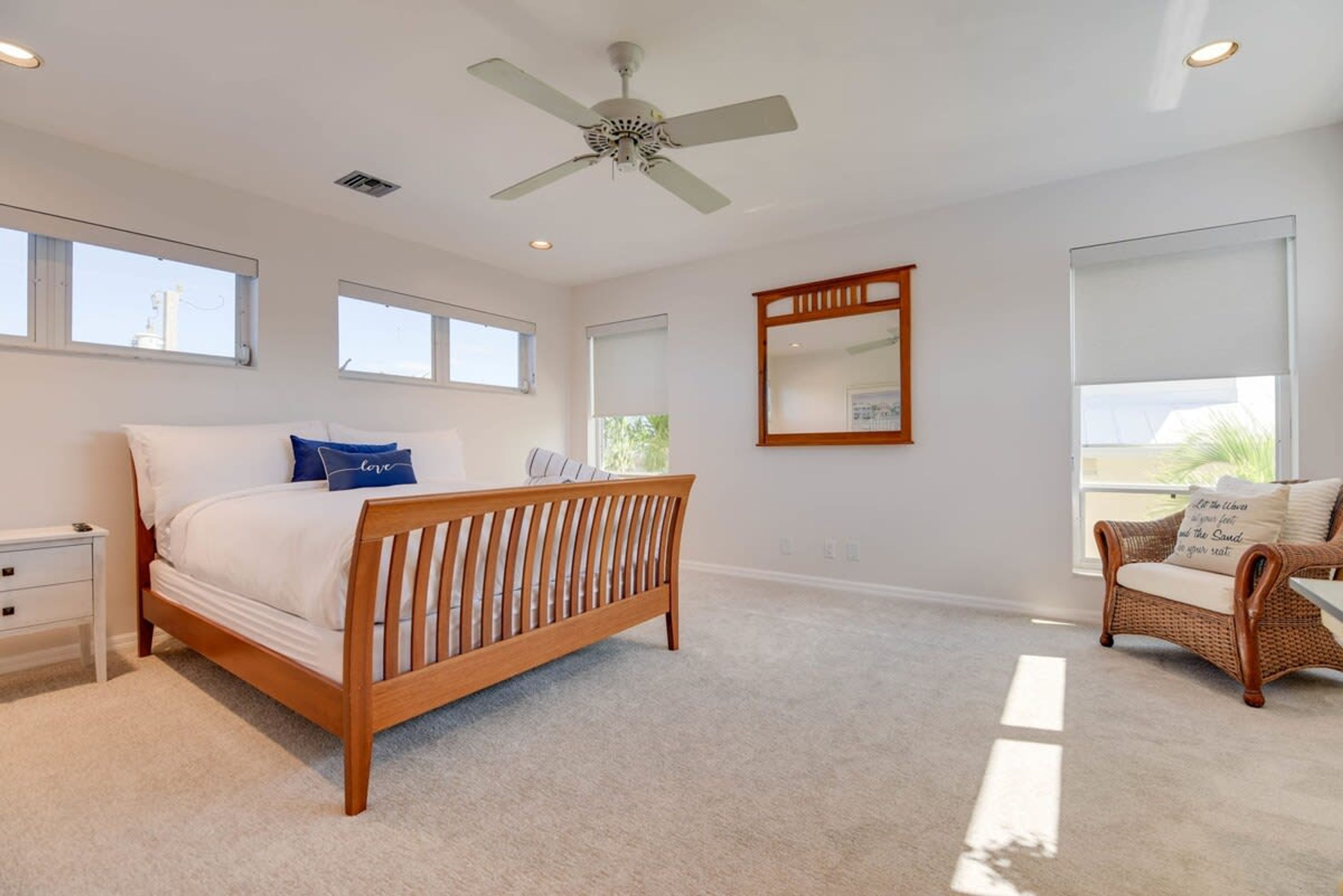 A bedroom with a wooden bed, a nightstand, a wicker chair, and a ceiling fan.