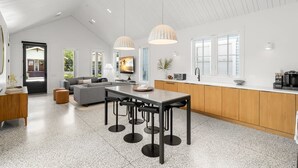 Un vaste espace de vie doté d’un haut plafond, une cuisine avec des meubles en bois et un coin repas agrémenté de tabourets de bar.
