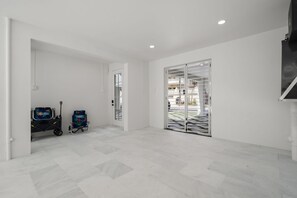 Una habitación amplia y moderna con suelo de baldosas, un gran ventanal corredero que da a un espacio exterior, y un cochecito de bebé en la esquina.