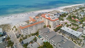 Vue aérienne d’une zone côtière avec une plage, des bâtiments et un hôtel à plusieurs étages, doté de toits rouges.