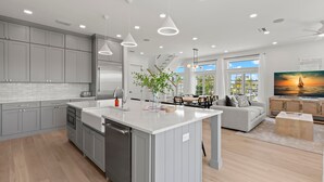 A modern kitchen with grey cabinets, a central island, and pendant lighting. - The Gemma Collection - 4 Stunning CWB Pool Homes (Clearwater Beach)
