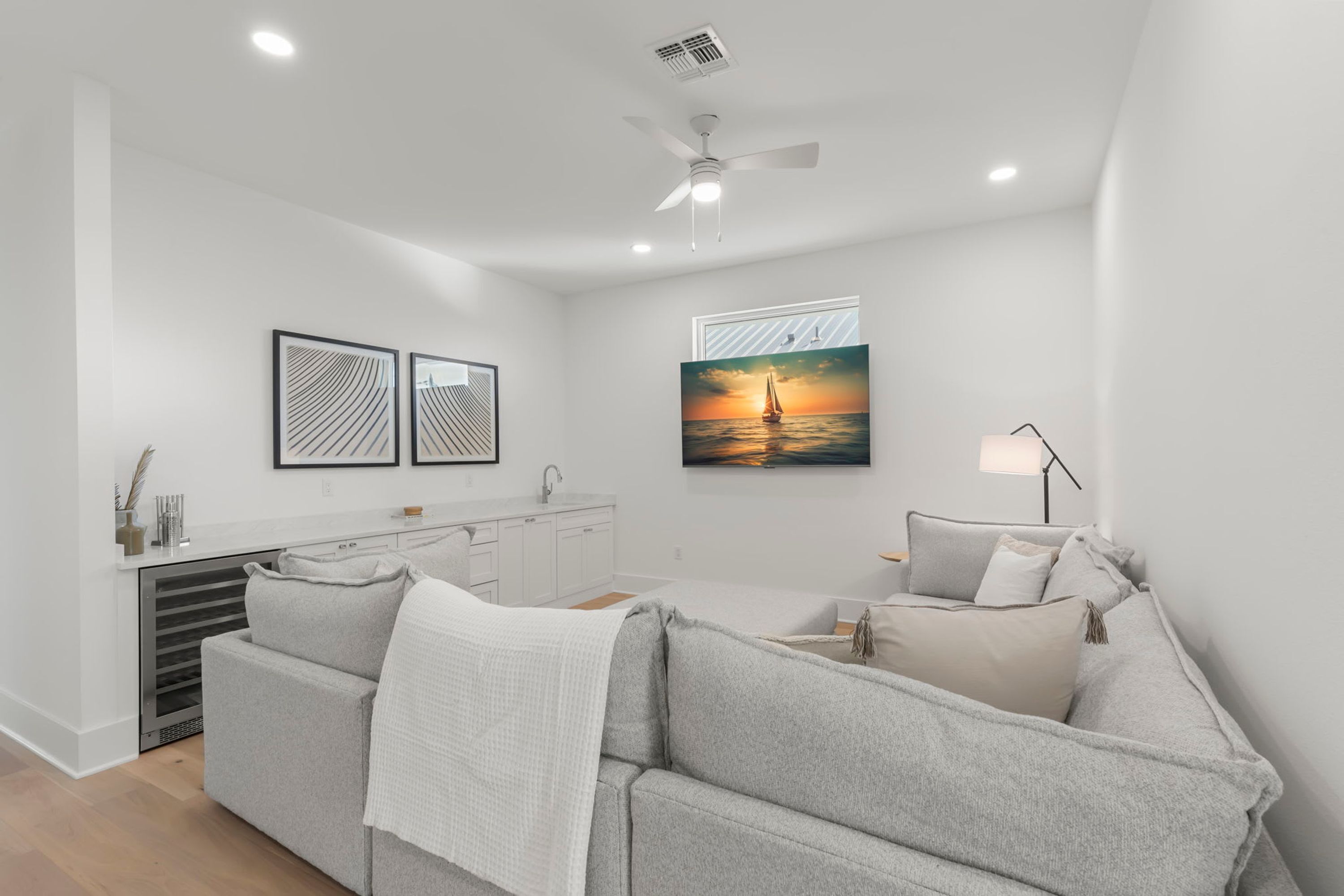 A modern living room with a grey sofa, a dining area with a white table, and a painting of a sunset over water.