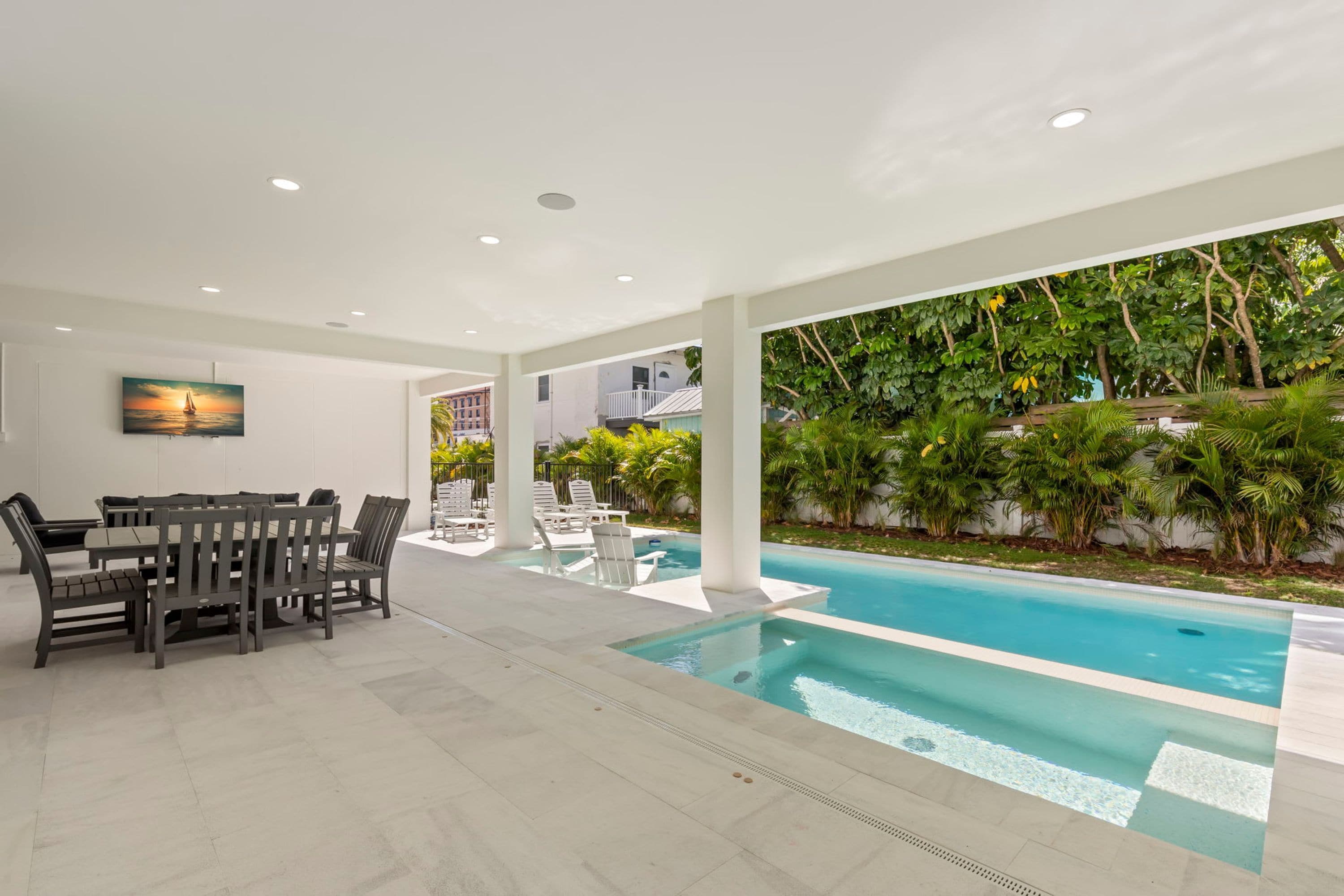 Un espace piscine intérieur moderne, doté d’une table et de chaises, entouré d’une végétation luxuriante et bordé d’une piscine à l’eau cristalline.