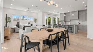 A modern kitchen with white cabinets, a central island, and a dining area with a wooden table and chairs. - Two Amazing Homes at The Gemma (Clearwater Beach)