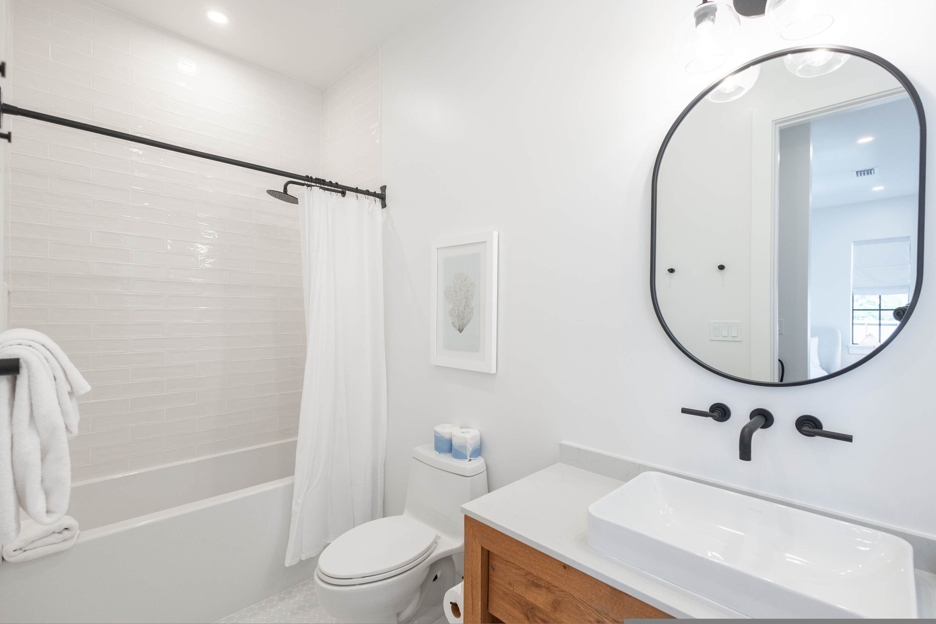 A modern bathroom with a white bathtub, a toilet, and a sink with a mirror above it.