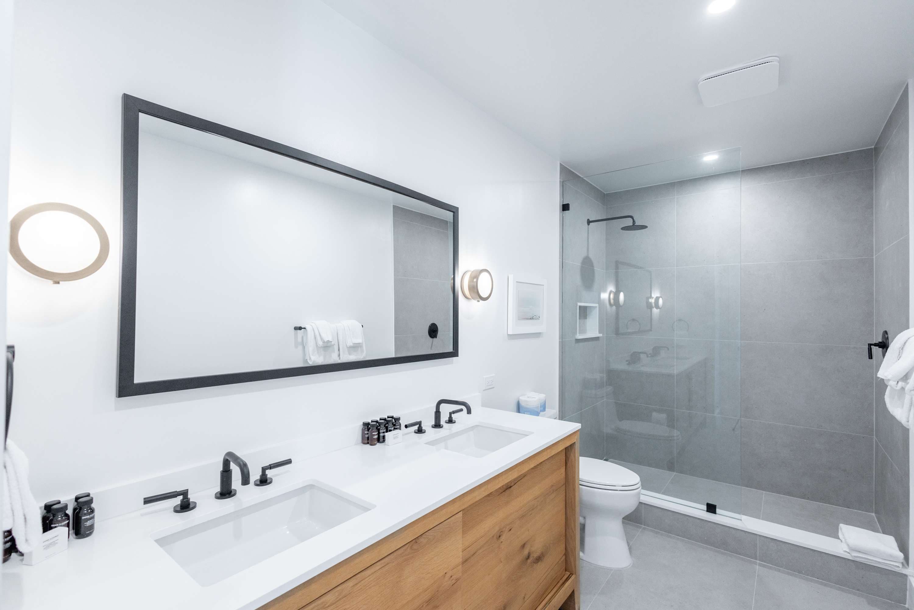 Une salle de bain moderne avec un grand miroir, deux lavabos, des toilettes et une douche à parois de verre.