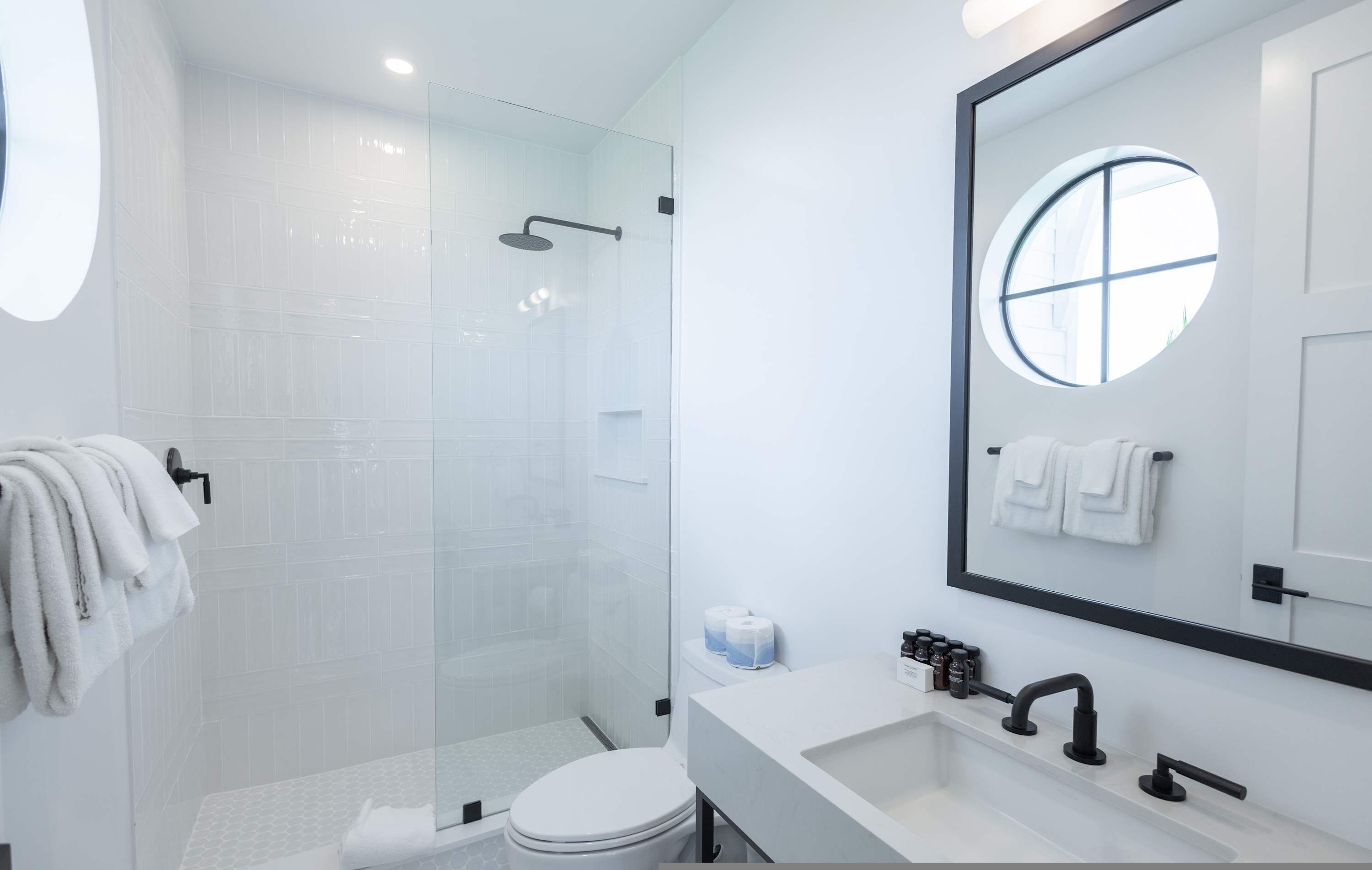A modern bathroom with a glass-enclosed shower, a white toilet, a sink with a mirror, and towels hanging on a rack.