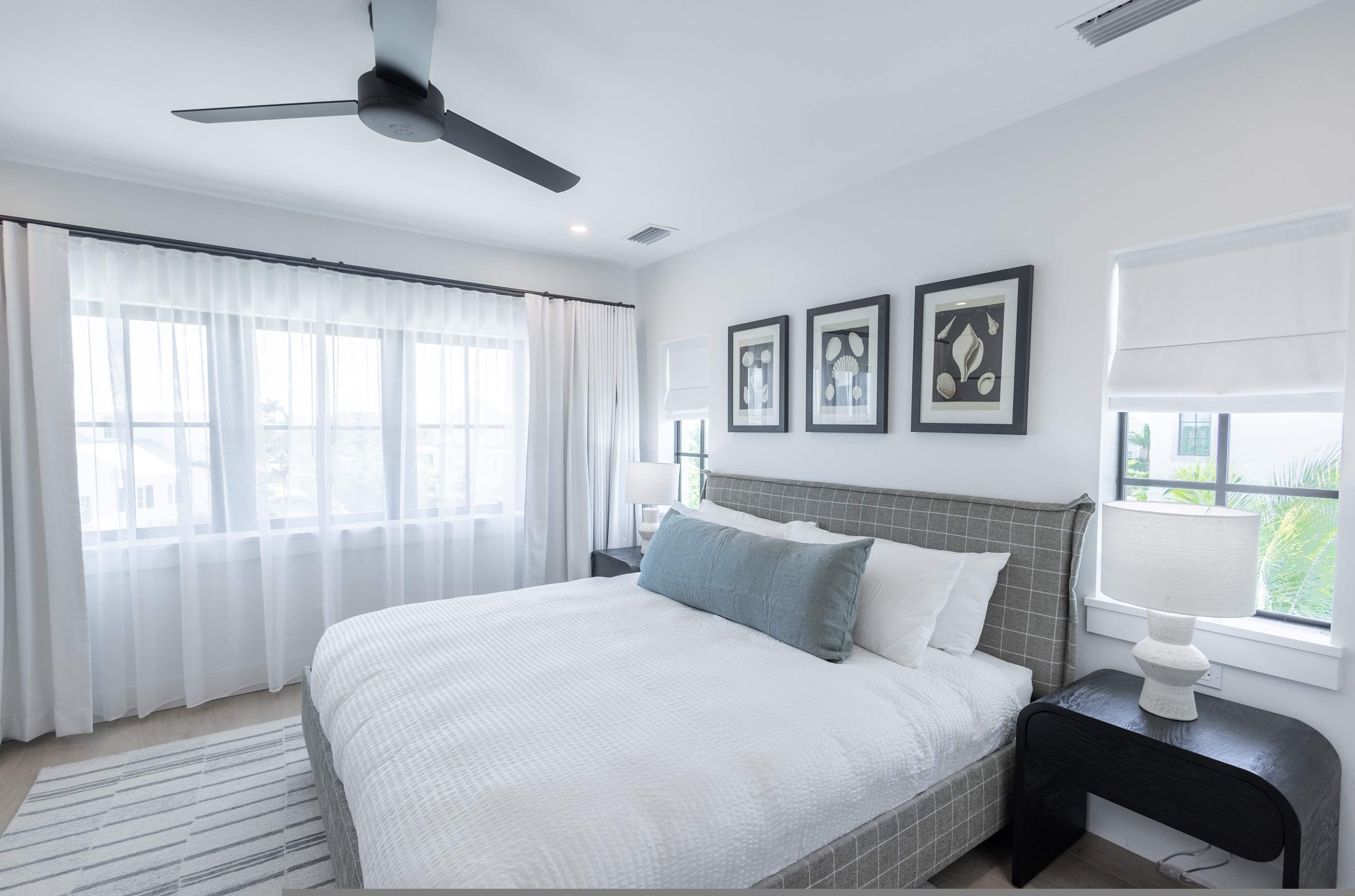 A modern bedroom with a large bed, a ceiling fan, and a window with curtains.