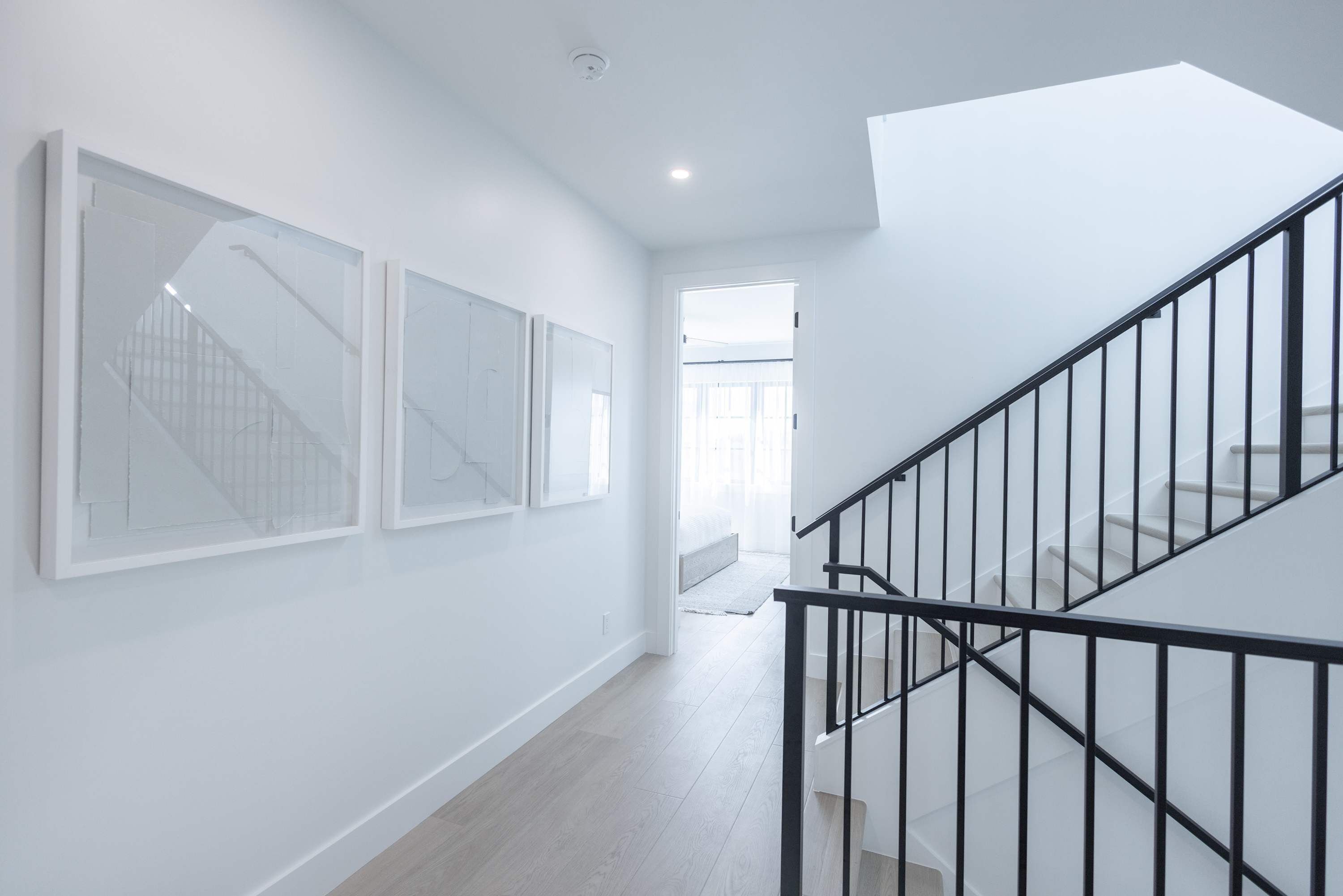 A modern interior with a staircase, white walls, and a hallway leading to a room with a bed.