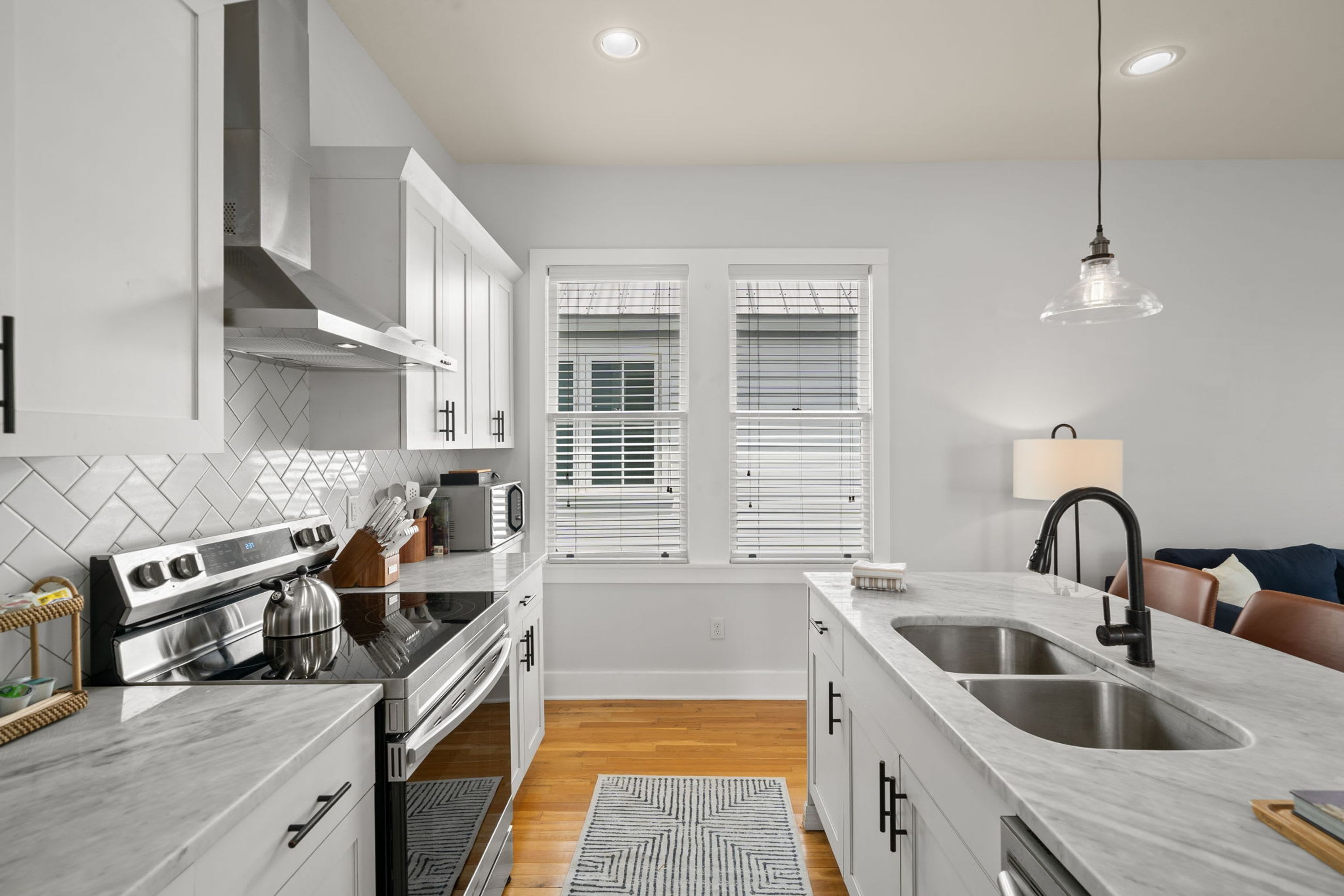 A modern kitchen with white cabinetry, a stainless steel stove, and a large island with a sink.