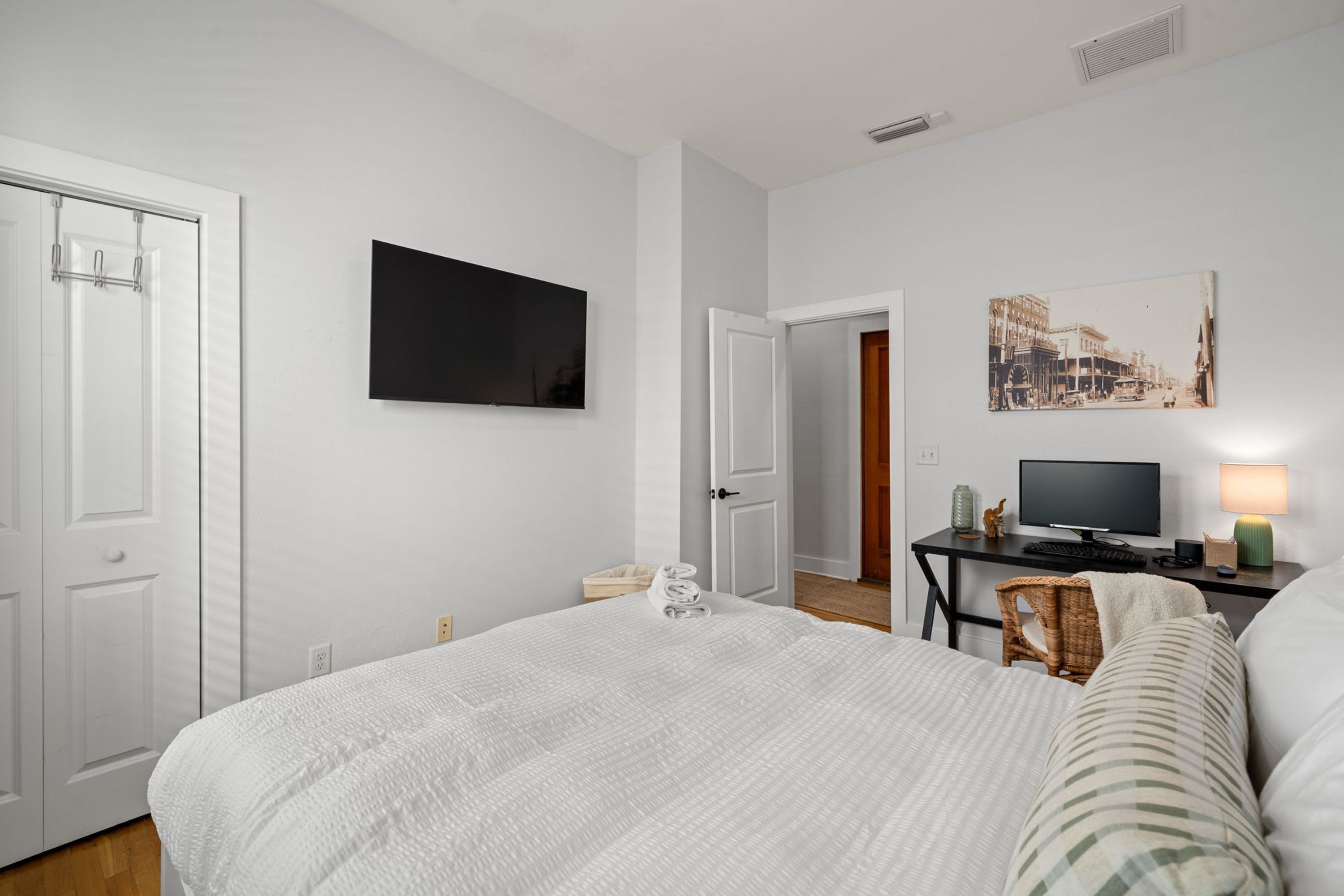 Une chambre avec un grand lit, un téléviseur fixé au mur, un bureau avec une lampe et un tableau accroché au mur.