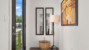 A hallway with a wicker basket, two framed mirrors, a floor lamp, and a painting on the wall. - NEW Soho Oasis - Stunning Home In Heart of Soho (Tampa)