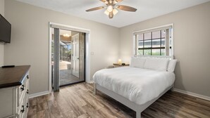 A bedroom with a bed, a ceiling fan, a window, and a door leading to a balcony. - NEW Surfside Beach House Heated Pool Boat Dock (Apollo Beach)