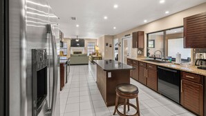 A modern kitchen with a central island, stainless steel appliances, wooden cabinets, and a tiled floor. - NEW Surfside Beach House Heated Pool Boat Dock (Apollo Beach)