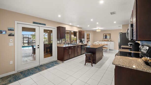 A modern kitchen with a large island, dark wooden cabinets, and a view of a pool through glass doors. - NEW Surfside Beach House Heated Pool Boat Dock (Apollo Beach)